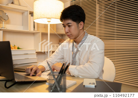 Working in the middle of the night, Man sat typing away on a laptop in his office with a determined look on his face, Male hand pressing on laptop keyboard. 110492177