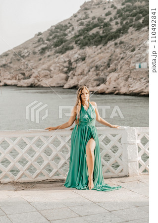 Woman sea green dress. Side view a happy woman with long hair in a long mint dress posing on a beach with calm sea bokeh lights on sunny day. Girl on the nature on blue sky background. 110492841