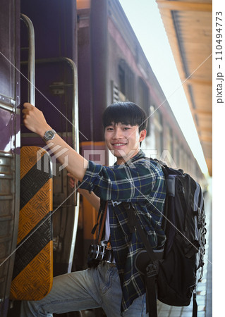 Portrait of happy male traveler with a backpack getting on the train. Travel and vacations concept. Portrait of happy male traveler with a backpack getting on the train. Travel and vacations concept. 110494773