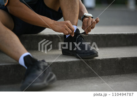 Young sporty man tying shoelaces getting ready for jogging outdoors. Healthy lifestyle concept 110494787