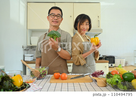 Beautiful senior couple cooking in cozy kitchen with fresh organic vegetables on table. Healthy eating concept 110494795