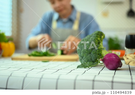 Select focus fresh vegetables on kitchen table with blurred senior man cooking in background 110494839