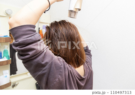 洗面所でドライヤーで髪の毛を乾かす女性 110497313
