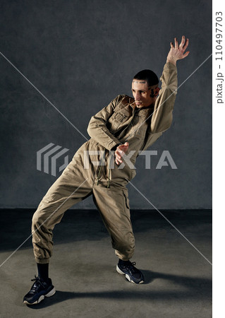 Stately guy with tattooed body and face, earrings, beard. Dressed in khaki overalls and black sneakers. Dancing on gray background. Dancehall, hip-hop Stately guy with tattooed body and face, earrings, beard. Dressed in khaki overalls and black sneakers. Dancing on gray background. Dancehall, hip-hop 110497703