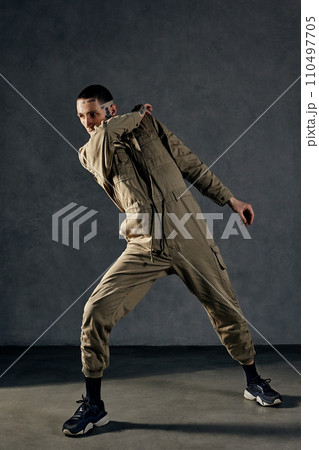 Stately male with tattooed body and face, earrings, beard. Dressed in khaki jumpsuit, black sneakers. Dancing on gray background. Dancehall, hip-hop Stately male with tattooed body and face, earrings, beard. Dressed in khaki jumpsuit, black sneakers. Dancing on gray background. Dancehall, hip-hop 110497705