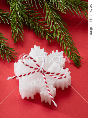 One white scented candle in the shape of a snowflake and a fir branch on a red background One white scented candle in the shape of a snowflake and a fir branch on a red background 110498703