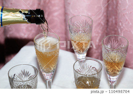 The process of pouring champagne into crystal glasses against a curtain, a nineties-style concept The process of pouring champagne into crystal glasses against a curtain, a nineties-style concept 110498704