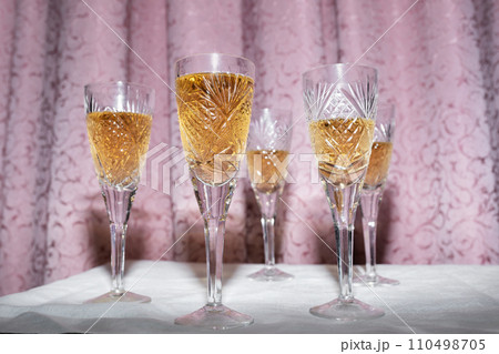 Five crystal glasses with champagne on a curtain background, nineties style concept Five crystal glasses with champagne on a curtain background, nineties style concept 110498705