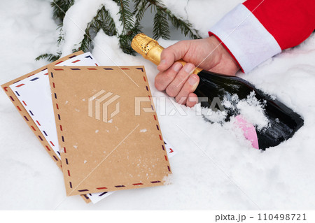Christmas letters and Santa Claus hand with a bottle of champagne on the snow, concept on the theme of bad Santa losing children's letters 110498721
