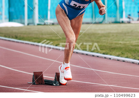 senior woman runner running from starting blocks sprint race in masters athletics 110499623