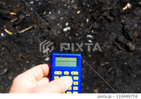 Blue calculator in dark soil, burnt ground after the fire 110499758