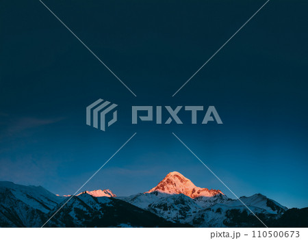 Georgia. Mount Kazbek Covered Snow In Winter Sunrise. Morning Dawn Colored Top Of Mountain In Pink-orange Colors. Awesome Winter Georgian Nature Landscape. Georgia. Mount Kazbek Covered Snow In Winter Sunrise. Morning Dawn Colored Top Of Mountain In Pink-orange Colors. Awesome Winter Georgian Nature Landscape. 110500673