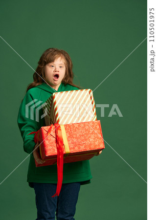 Emotional teen girl with down syndrome standing with socked face, holding many present boxes against green studio background 110501975