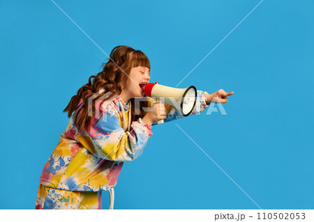 Health care awareness. Teen girl with down syndrome shouting in megaphone against blue studio background Health care awareness. Teen girl with down syndrome shouting in megaphone against blue studio background 110502053