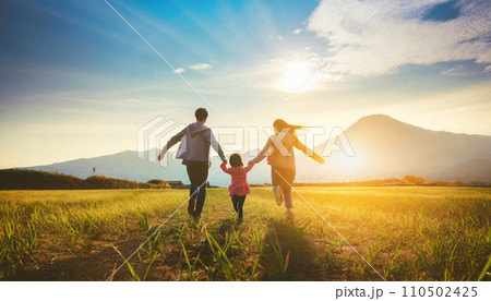 家族が仲良く手をつなぎ、青空と草原の中を走る後ろ姿のAI画像 110502425