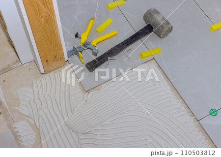 During installation of large tiles, tiler works over mortar adhesive that bonds ceramic floor tile together During installation of large tiles, tiler works over mortar adhesive that bonds ceramic floor tile together 110503812
