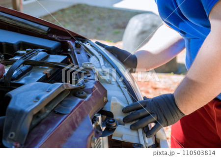 During car repair, mechanic assembles headlight on an automobile During car repair, mechanic assembles headlight on an automobile 110503814