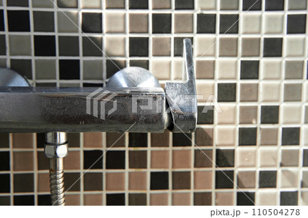 Limescale on the dirty faucet switch in the shower room. Brown tiles on the wall. 110504278