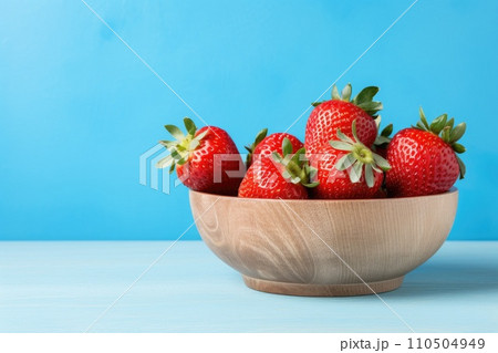 Fresh juicy strawberries in wood bowl on light blue table Fresh juicy strawberries in wood bowl on light blue table 110504949