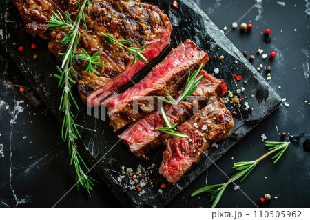 Sliced grilled meat steak with spices rosemary and pepper on black marble board 110505962
