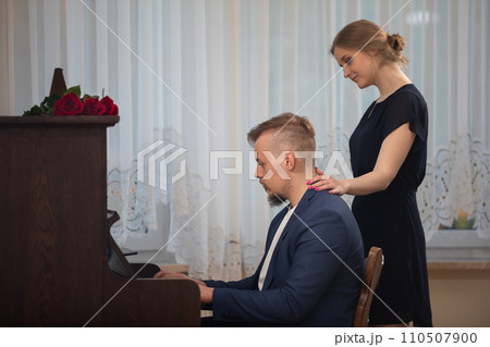 A musician plays the piano while his woman walks by. 110507900