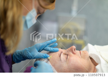The beautician inserts a needle into the client's forehead to introduce the product under the skin. The beautician inserts a needle into the client's forehead to introduce the product under the skin. 110507913
