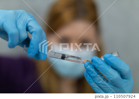 The woman holds her hands in front of her and holds a syringe and a vial in them. The woman holds her hands in front of her and holds a syringe and a vial in them. 110507924