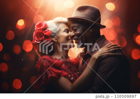 Affectionate senior mixed race couple embraced in a romantic setting of pink flowers on black background. Affectionate senior mixed race couple embraced in a romantic setting of pink flowers on black background. 110509897