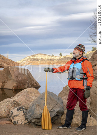 senior male paddler with a wooden canoe paddle on a rock shore of a mountain lake - Horsetooth Reservoir in fall or winter scenery senior male paddler with a wooden canoe paddle on a rock shore of a mountain lake - Horsetooth Reservoir in fall or winter scenery 110510616