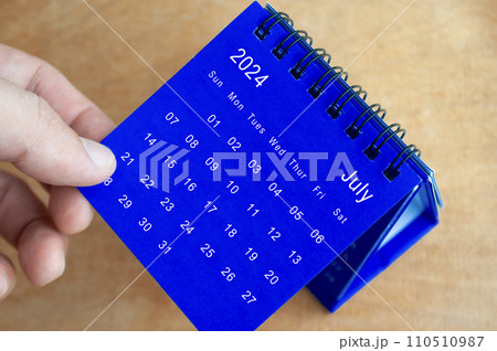 Hand showing July 2024 table calendar on wooden background. Calendar and new month concept. 110510987
