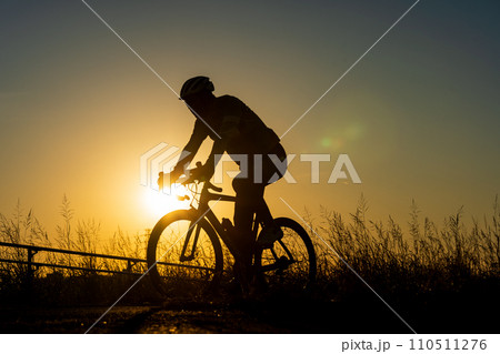 夕日とロードバイクに乗る人のシルエット 110511276