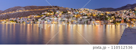 Multi-colored facades of houses in the light of lanterns in the village of Symi at sunset. 110512536