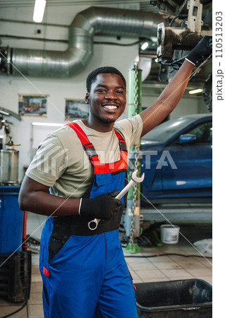 Portrait of young african man car service worker wearing uniform standing in garage Portrait of young african man car service worker wearing uniform standing in garage 110513203
