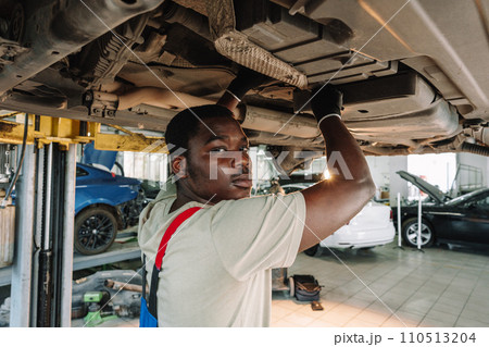 Young African mechanic in uniform working under the car in car service center Young African mechanic in uniform working under the car in car service center 110513204