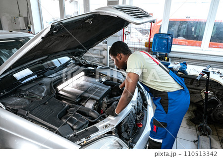 Young African man working under the hood of car fixing engine in auto service Young African man working under the hood of car fixing engine in auto service 110513342