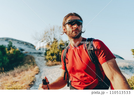 Young man hiker travels through the mountains with trekking poles for nordic walking Young man hiker travels through the mountains with trekking poles for nordic walking 110513533