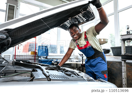 Young African man working under the hood of car fixing engine in auto service Young African man working under the hood of car fixing engine in auto service 110513696