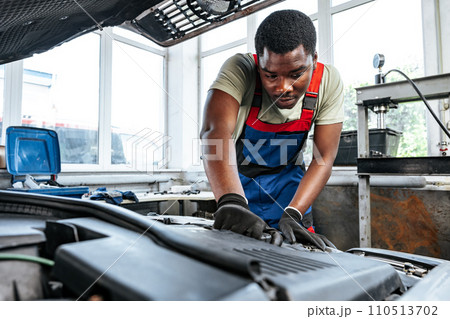 Young African man working under the hood of car fixing engine in auto service 110513702