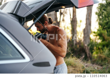Young man changing clothes on the car trunk after hiking in the woods 110514063