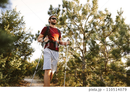 Young man hiker travels through the mountains with trekking poles for nordic walking Young man hiker travels through the mountains with trekking poles for nordic walking 110514079