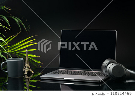 Laptop with black screen on working desk with cup and earphones on black background 110514469