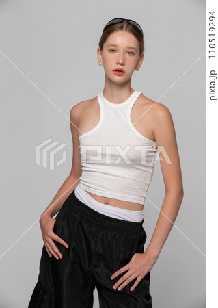 A young beautiful girl fashion model in a white top is posing on a gray background. 110519294