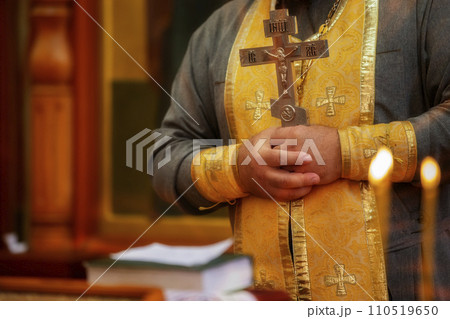The priest's hands hold a cross against a background of flickering candles. Religion and faith. 110519650