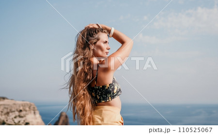 Woman travel sea. Happy tourist taking picture outdoors for memories. Woman traveler looks at the edge of the cliff on the sea bay of mountains, sharing travel adventure journey 110525067