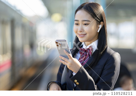 スマートホンの画面を見るイヤホンをつけた女子高校生　手元フォーカス 110528211