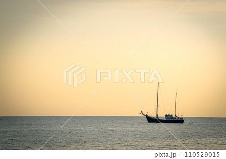 Yacht resting on sea water in sunset light with a tiny still visible plane rising from the nice airport 110529015