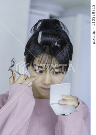 カーラーを巻いてまつ毛にビューラーをする若い女性　縦位置 110529515