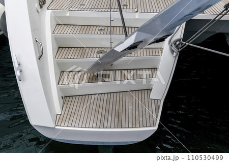 Stern of super luxury yacht berthed in marina. Teak deck on stern of sailing boat. Teak stairs ladder on motor boat. Aft part. Yachting concept. 110530499