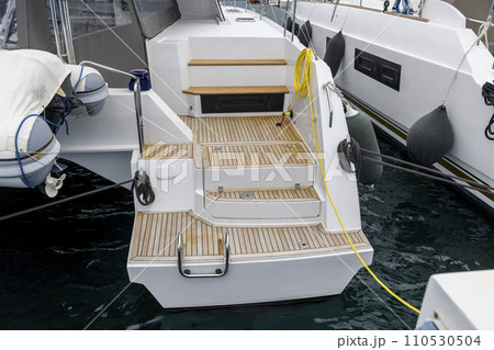 Stern of super luxury yacht berthed in marina. Teak deck on stern of sailing boat. Teak stairs ladder on motor boat. Aft part. Yachting concept. Stern of super luxury yacht berthed in marina. Teak deck on stern of sailing boat. Teak stairs ladder on motor boat. Aft part. Yachting concept. 110530504