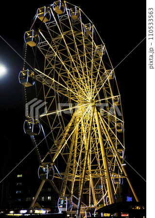 Part of ferris wheel against a blue sky background with lights neby night lighting 110533563